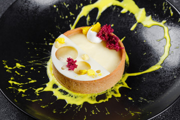 Lemon tart on a black plate. Beautiful serve from the cook in a restaurant.