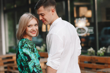 Love story, a man and a blonde girl. Loving couple sitting hugging, kissing, looking at each other, smiling and laughing, on a European city street in the summer. In casual wear. 