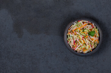 Salad of fresh vegetables radish, cucumber, carrots with parsley and green onions in a wooden bowl on a dark background top view copy space