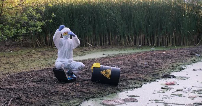 A scientist in a protective suit takes samples in the technogenic pollution zone near the black barrel.