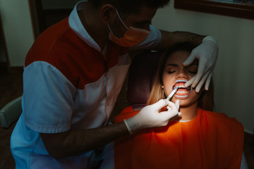 A beautiful caucasian woman is sitting in a chair in the dentist's office while the young dentist examines her teeth