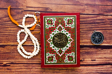 Quran is your guidance of your life concept with the Koran, prayer beads and compass. Large writen Arabic word mentioned Holy Quran is with variance recitation and correct pronounciations method. - obrazy, fototapety, plakaty