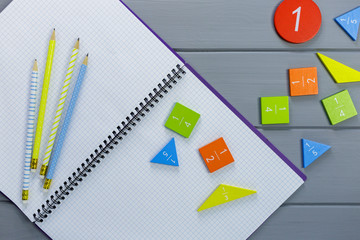 Colorful math fractions, numbers on open notebook and pencils on gray wooden background....