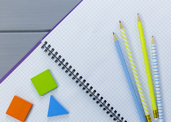 Colorful math fractions, numbers on open notebook and pencils on gray wooden background....