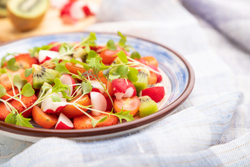 Vegetarian fruits and vegetables salad of strawberry, kiwi, tomatoes, microgreen sprouts on white concrete background. Side view, selective focus.