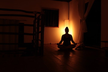 Silhueta de Mulher sentada no chão meditando no escuro