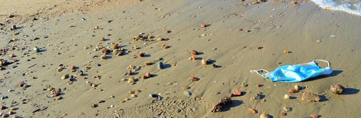 disposable face mask with small stones on the beach 
