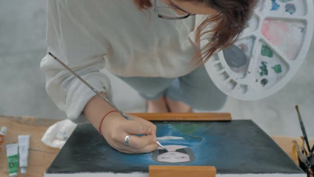 vista desde arriba de pintora frente a un caballete y cuadro pintando retarto