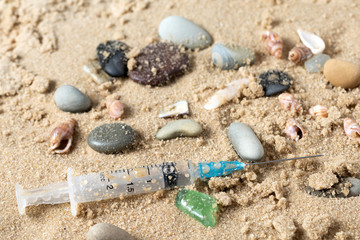 Syringes with needles and plastic trash on the beach near the sea