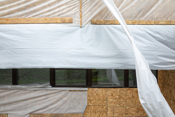 Exterior plywood wall covered in plastic sheeting during a construction work stoppage