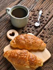 A cup of coffee with coffee beans and croissant on wooden table