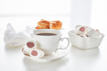 Still life with cup of coffee and bowls with marshmallows and croissants on light background. Sweet meal. Dessert