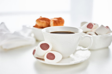 Still life with cup of coffee and bowls with marshmallows and croissants on light background. Sweet meal. Dessert
