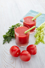 Two glasses with fresh tomato juice and ripe tomatoes  on light wooden background. Top view