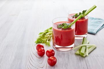 Two glasses with fresh tomato juice and ripe tomatoes  on light wooden background. Top view