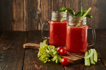 Two glasses with fresh tomato juice, celery, parsley and ripe tomatoes on dark brown wooden background.