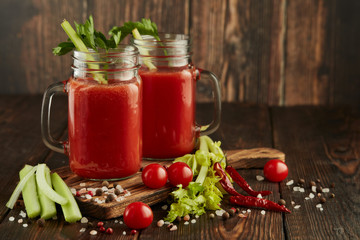 Two glasses with fresh tomato juice, celery, parsley and ripe tomatoes on dark brown wooden background.
