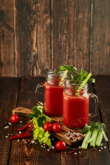 Two glasses with fresh tomato juice, celery, parsley and ripe tomatoes on dark brown wooden background.