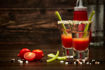 Two shot glasses with cocktail Bloody Mary on dark wooden background with copy space
