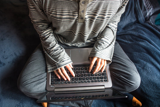 Bird's Eye Angle Photography Of A Homeoffice With A Young Man In Gray Striped Pajamas And Orange Stockings Studying/working With A Laptop On His Legs. Dark Blue Blanket Background.