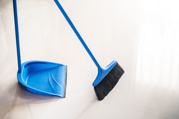 Sweeping broom and dustpan on bright shiny tile floor