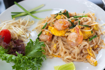 Pad Thai or Phad Thai, Thai style stir fried rice noodle with shrimp and egg, decorated with vegetables on white ceramic dish.