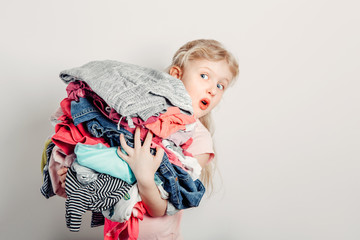Mommy little helper. Cute Caucasian girl sorting clothes. Adorable funny child arranging organazing clothing. Kid holding messy stack pile of clothes, things. Home chores housework.