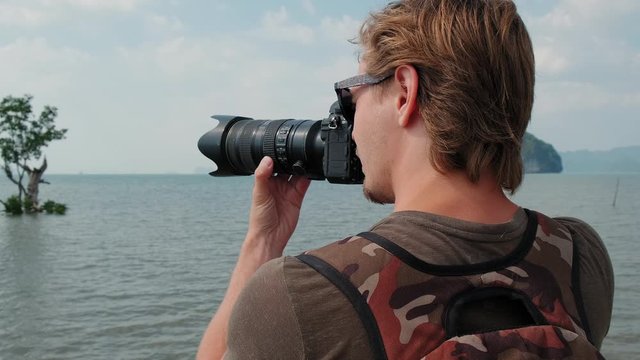 Close up portrait of a man taking photo on a professional camera. Photographer with backpack taking picture of scenic landscape near the sea. 4k, cinematic