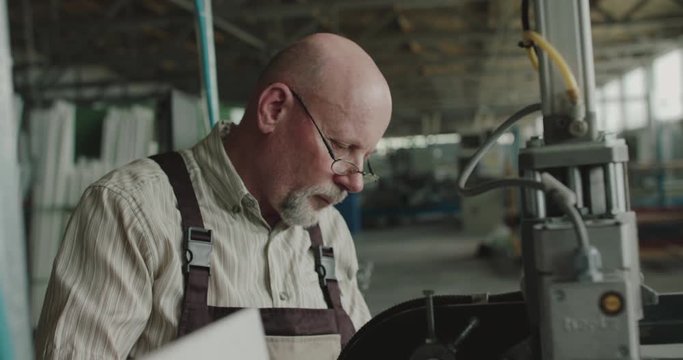 Thoughtful senior engineer examining machine, greeted to collaborator on factory