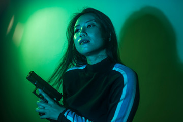 Obraz na płótnie Canvas cinematic portrait of young attractive and dangerous special agent woman spy or Asian Korean mobster girl holding handgun pointing the gun fierce in Hollywood style