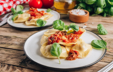 Italian ravioli with meat tomato sauce and basil leaves with on a white dishes on an old rustic background.