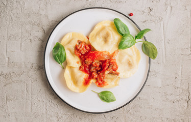 Italian ravioli with meat tomato sauce and basil leaves with on a white dishes on concrete background.