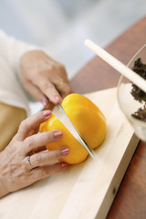Hand of senior woman cutting yellow capsicum