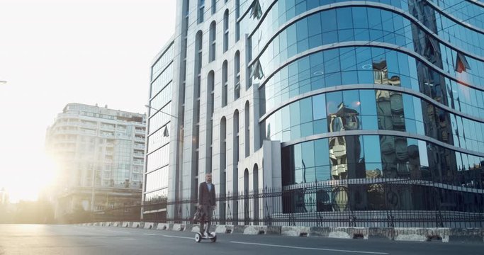 A man in a suit rides on a gyroboard and talks on the phone against the background of a business center.