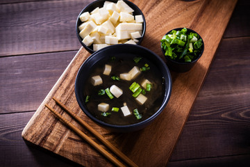 Japanese hot miso soup in a black bowl on the wooden table. Horizontal view from above.