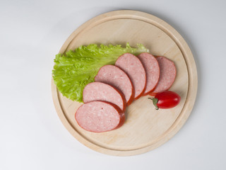 Raw smoked sausage, cut into slices on a board. Near leaf lettuce and tomato