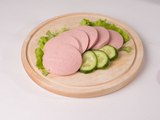 Boiled sausage, cut into slices on a board. Near lettuce leaf and fresh cucumber