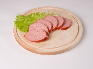 Raw smoked sausage, cut into slices on a board. Beside Lettuce Leaf