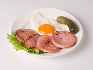 Fried sausage with fried eggs on a plate. Next to a lettuce leaf and pickle