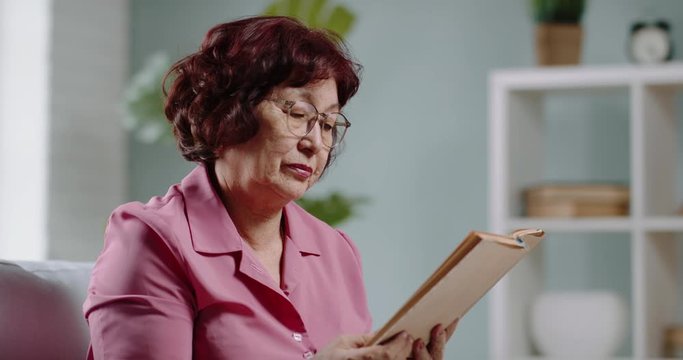 Sick senior asian woman sitting at home reading, suddenly sneezing and blowing nose into tissues, infected with virus - coronavirus, flu concept 4k footage