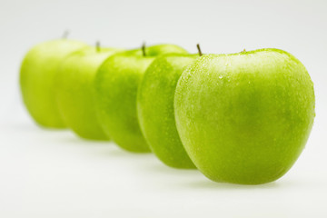 Green apples in a row with water droplets