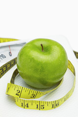 Measuring tape wound around a green apple on a weighing scale