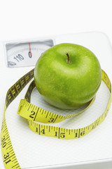 Measuring tape wound around a green apple on a weighing scale