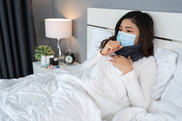 sick woman in medical mask coughing and suffering from virus disease and fever in bed, coronavirus (covid-19) pandemic concept