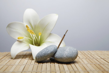A burning joss stick placed in between pebbles with a flower in the background