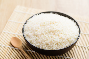 Organic Thai Jasmine rice grain in a bowl with spoon on wooden background