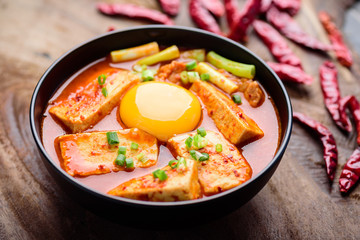 Kimchi soup with tofu and egg in a bowl on wooden background, Korean food (Kimchi Jjigae)