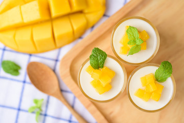 Thai dessert mango pudding, ripe mango dip in agar and coconut milk jelly on top in the glass decorated with mint leaf