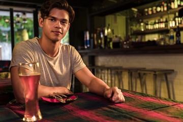 portrait of asian young man sitting in pub and restaurant and having beer