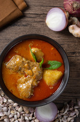 Chicken massaman curry in black bowl with herb and spices on wooden background. Thai authentic food called massaman kai. top view. Flat lay.